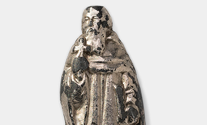 Modern photograph of a small silver-colored statuette depicting an old bearded man in robes
