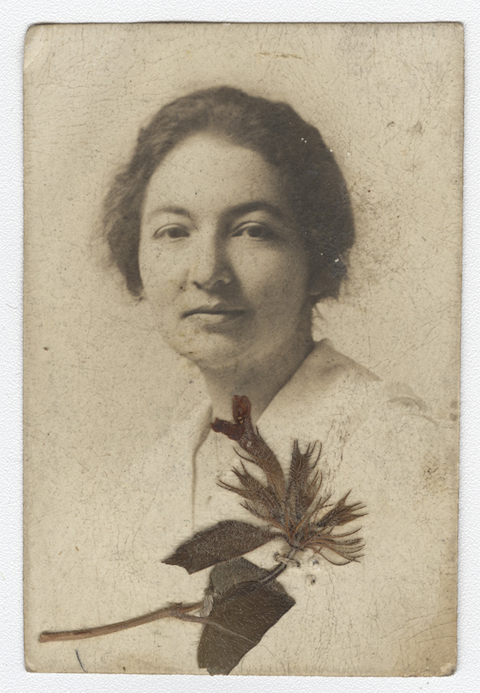 Sepia photograph of a young white woman. A dried flower rests at the bottom of the photo.