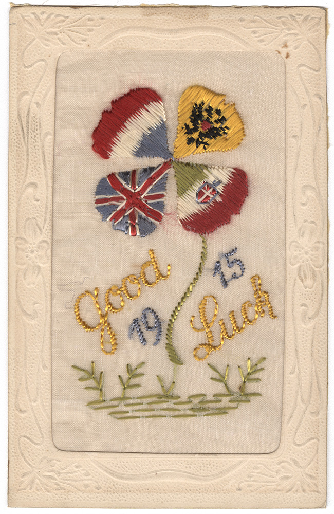 Scan of a postcard embroidered with a silk four-leaf clover. The four leaves are done in the designs and colors of the French, Russian, Italian and United Kingdom's WWI-era flags. The text "Good Luck 1915" is embroidered in gold and blue silk.