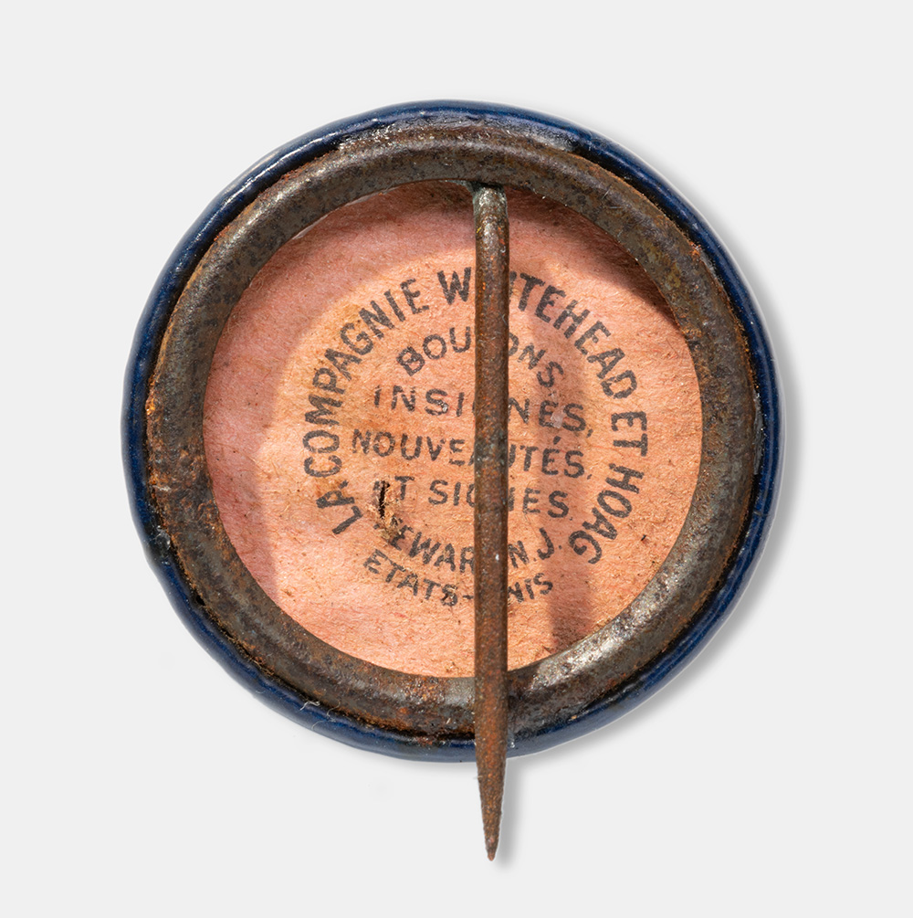 The back of a circular pin with a single pin fastener pointing downwards. Text printed on the back: 'La Compagnie Whitehead et Hoag'