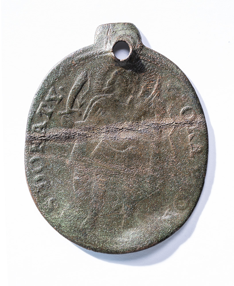 Dark grey-colored oval medal carved faintly with a human figure with wings and holding a sword