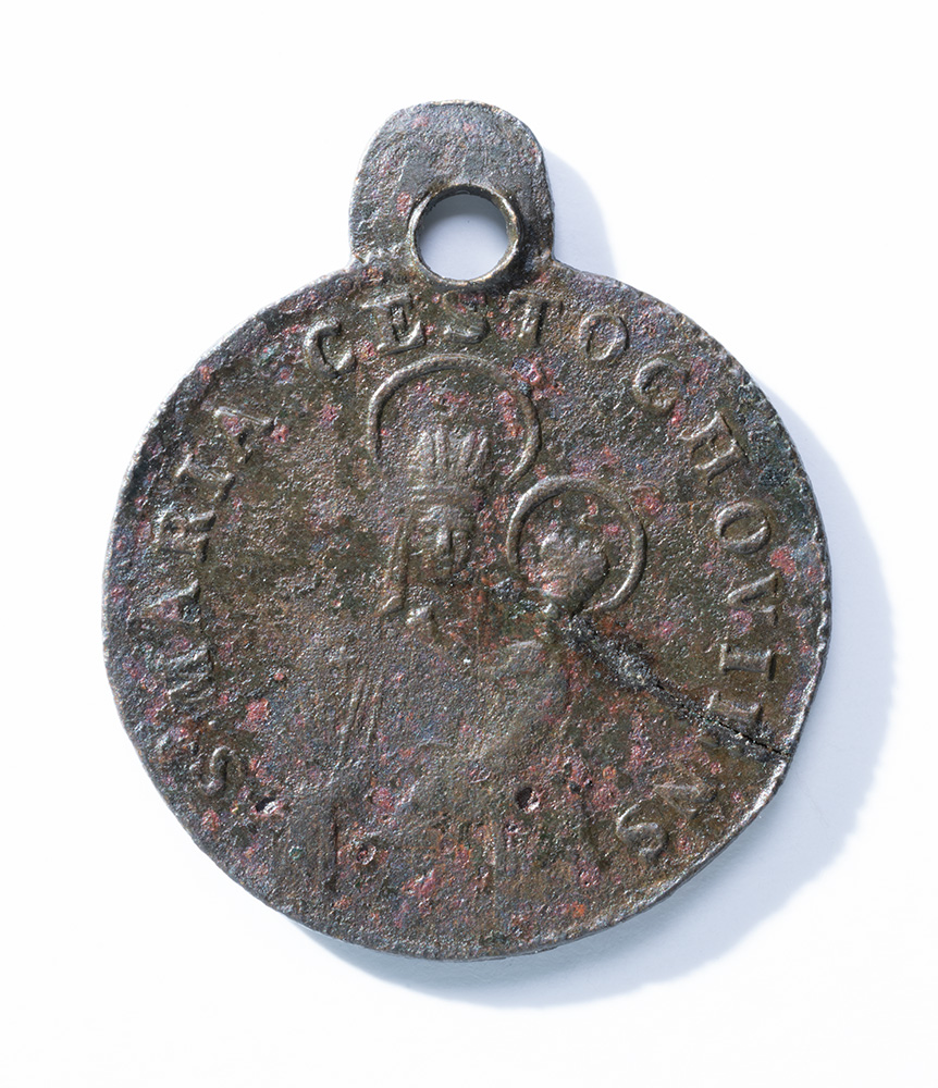 Grey and rusty circular medal depicting a woman holding an infant, both with halos around their heads.