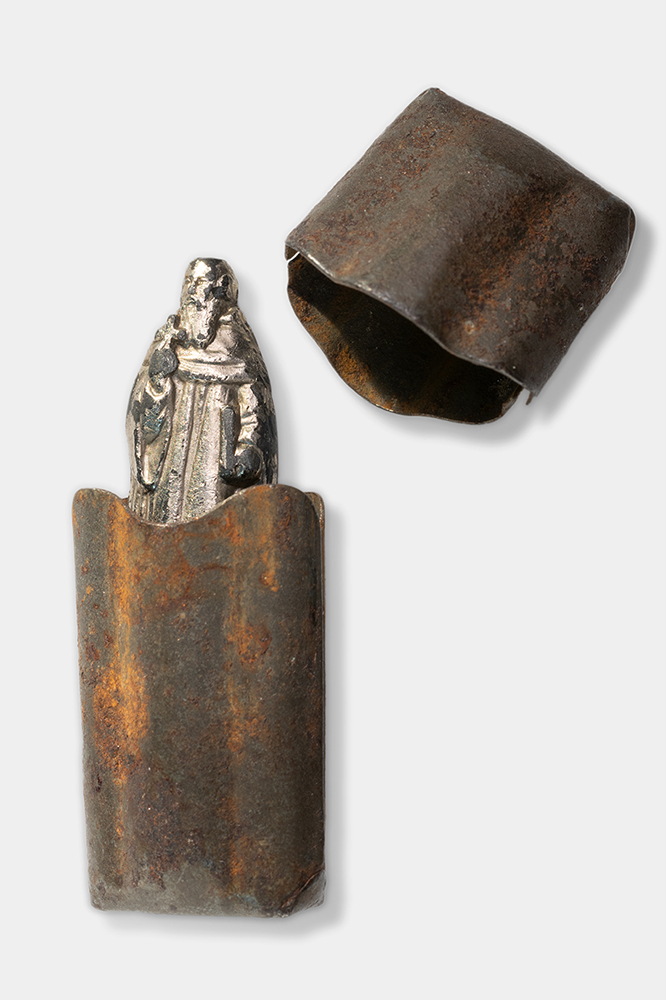 Silver-colored figurine of a bearded man in robes tucked halfway into a brown pouch or container.