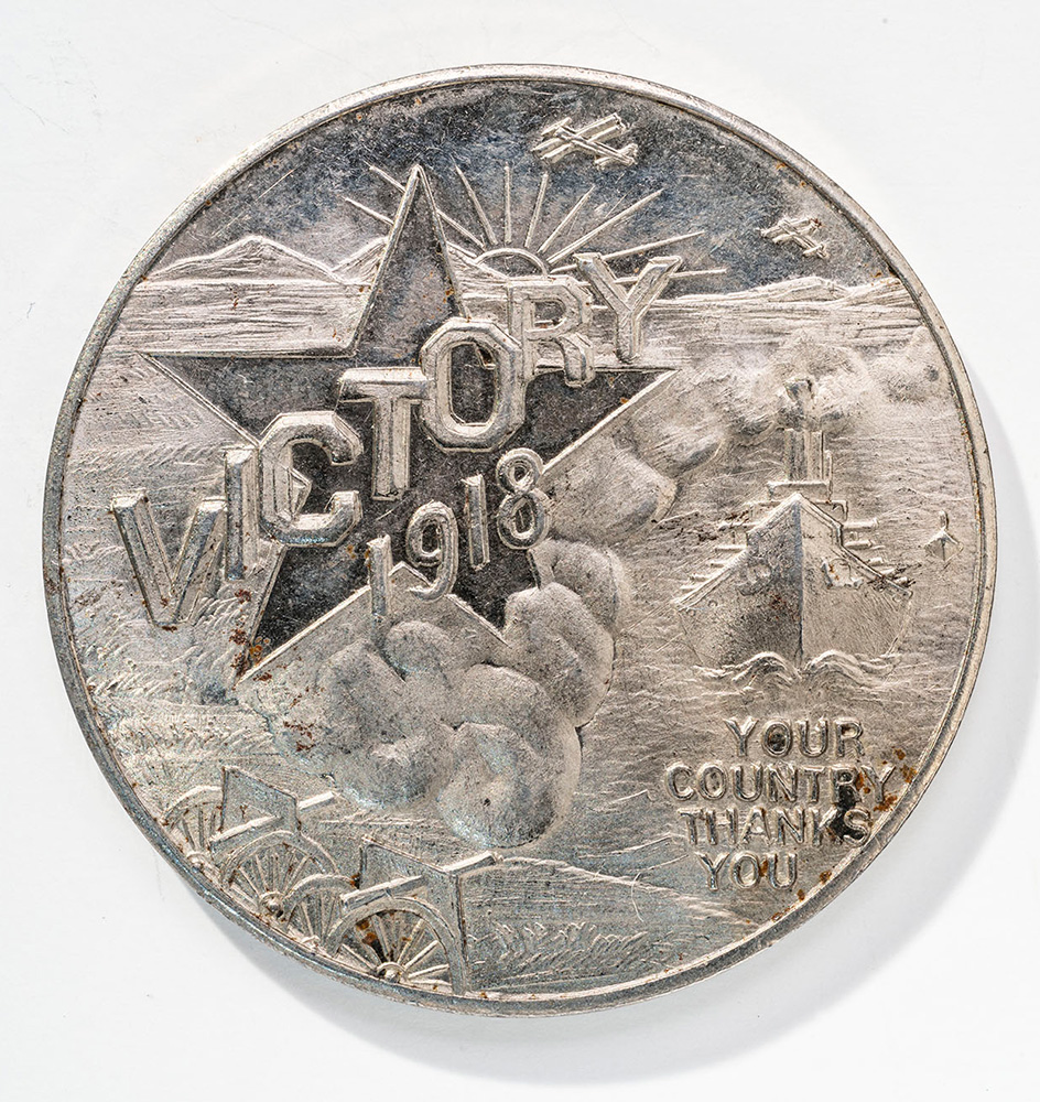 Silver-colored coin engraved with the sun, clouds and stars. Engraved text: 'VICTORY 1918'