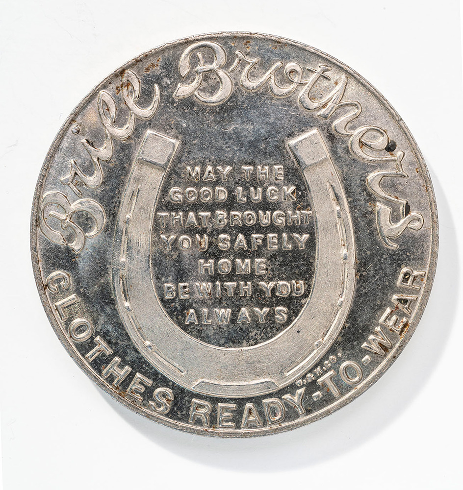 Silver-colored coin engraved with a horseshoe and some text in the center. Text around the border: 'Brill Brothers / Clothes Ready-to-Wear'