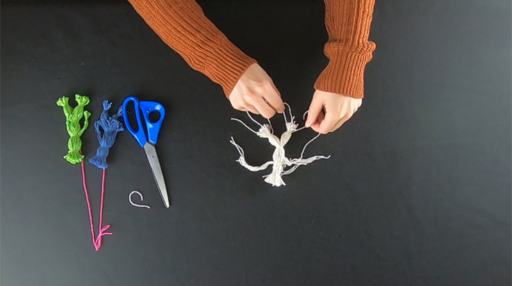 A person tying a piece of string around half of the bottom section of the looped bundle. The other leg has already been tied.