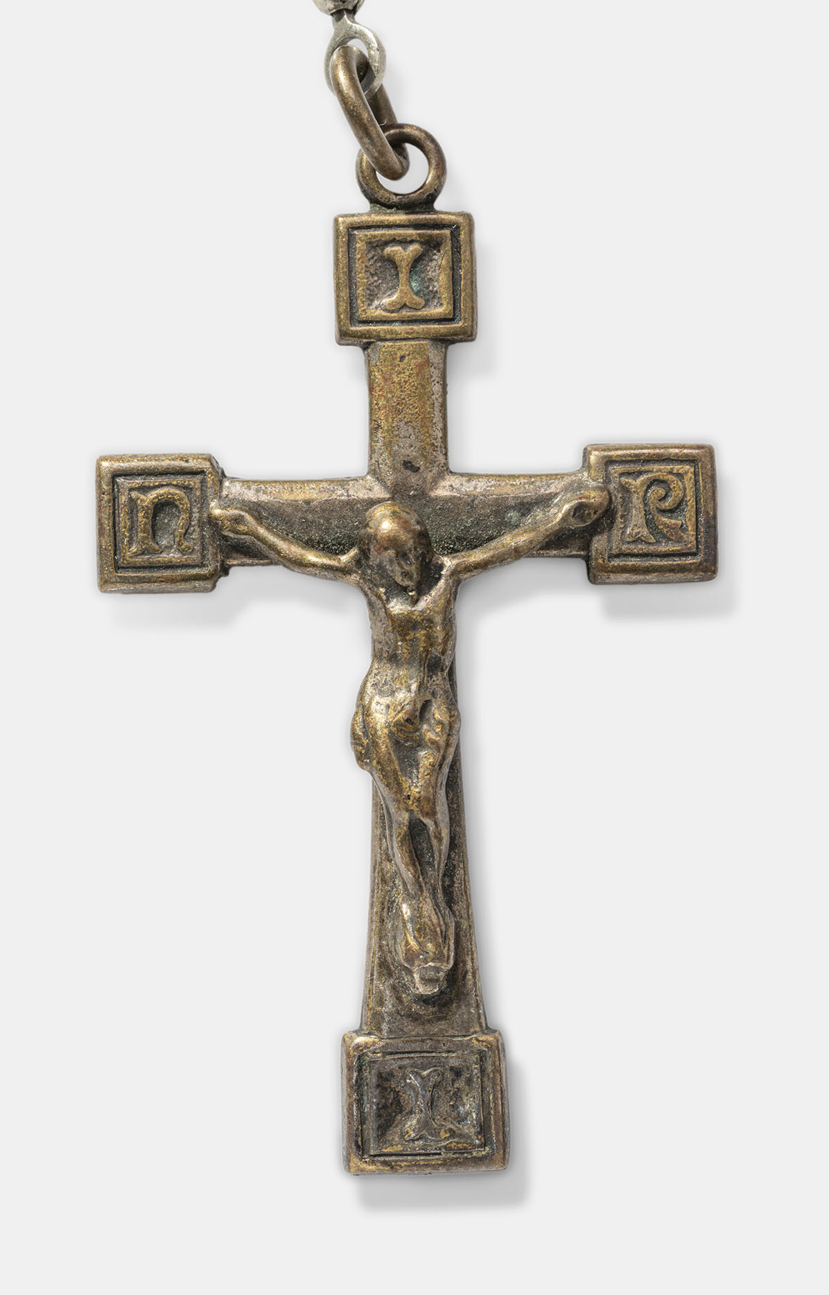 Close-up of a dull bronze-colored cross pendant with a crucified human on the front