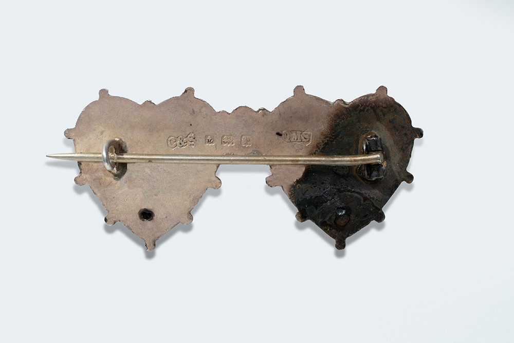Back of a silvery brooch with one horizontal pin fastener